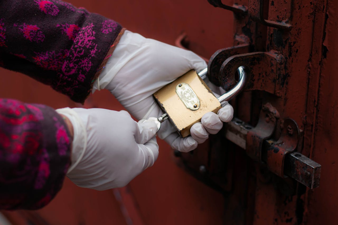 service-06 A close-up of gloved hands unlocking a rusty door padlock.